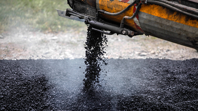 Svart asfaltsmassa på nyasfalterad väg