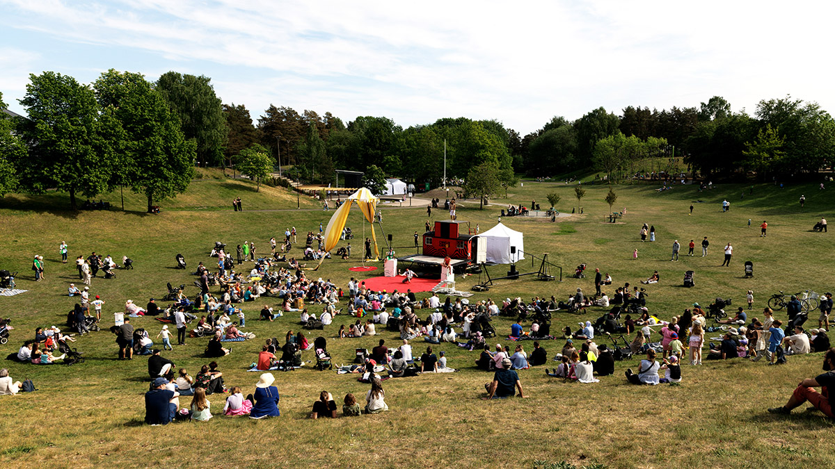 Vy över en grön park med folk sittandes i sluttningen