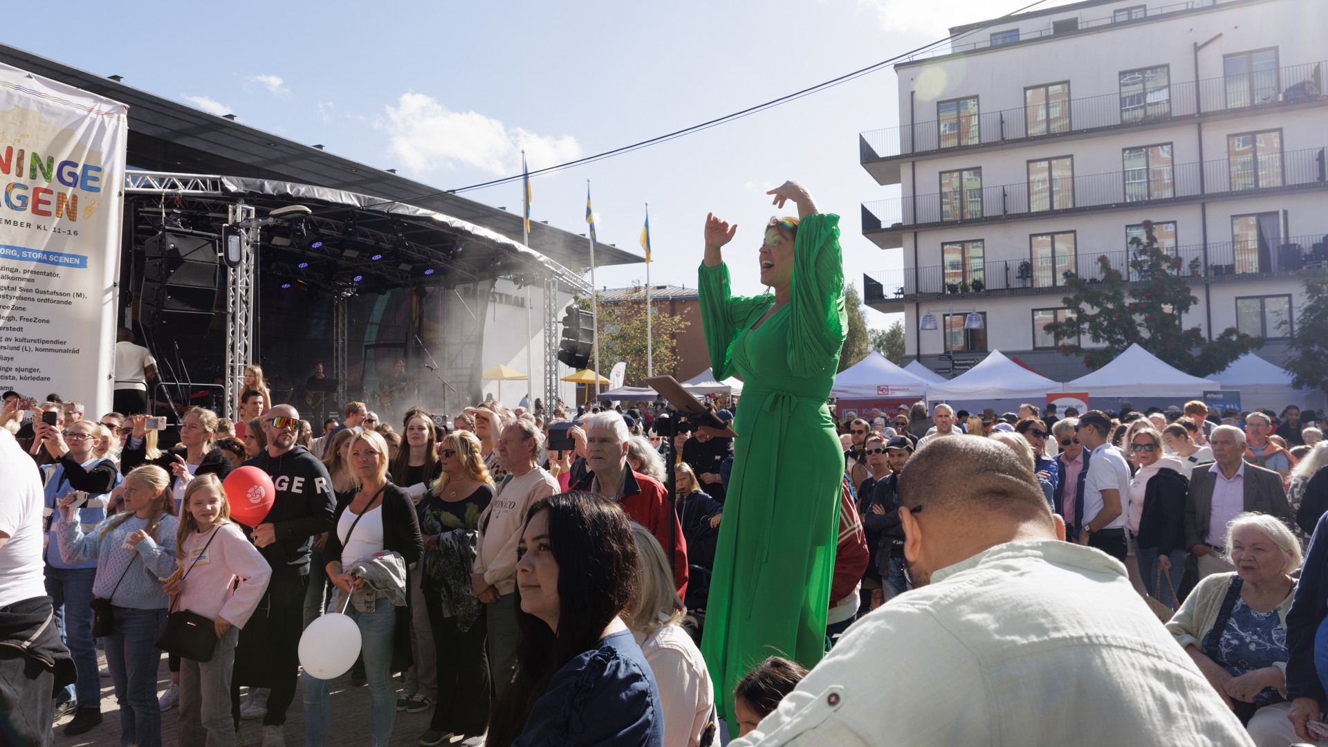 Kvinna i grön klänning står framför en folkmassa.