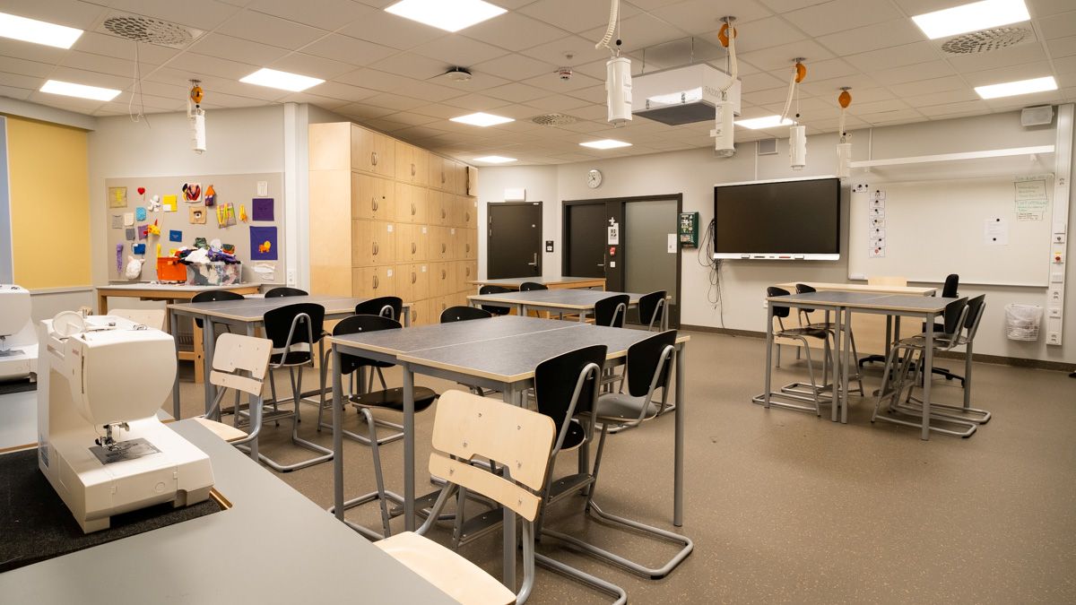 En textilsal med arbetsbord, symaskiner, förvaringsskåp och en stor digital skärm längst fram i rummet.