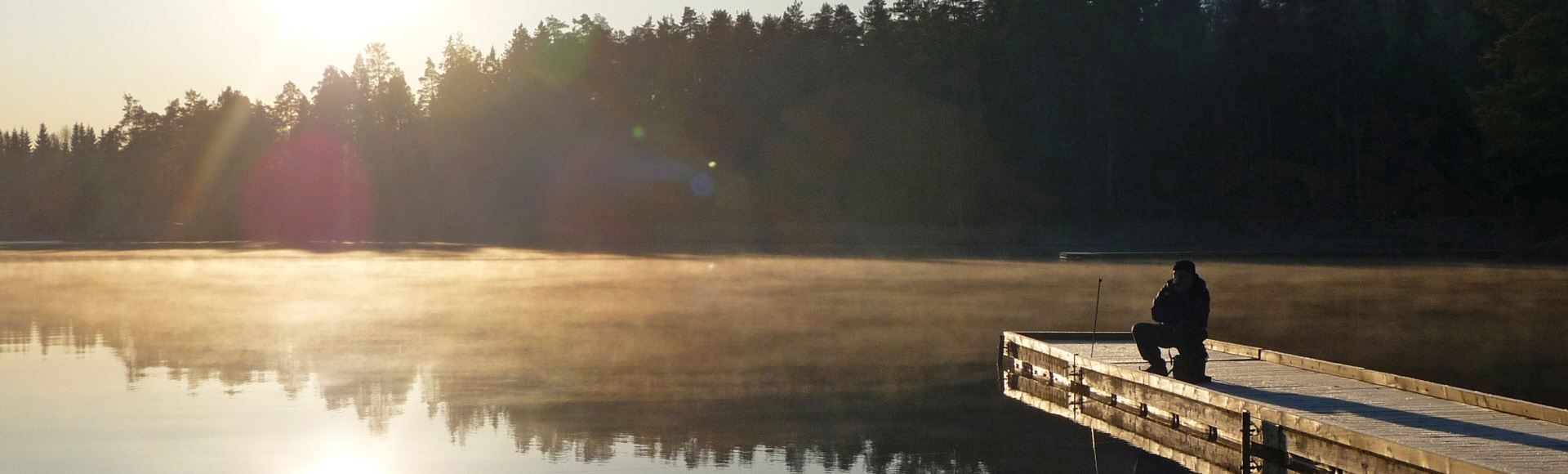 Bild på en brygga på Rudan med en man på knä som fiskar.