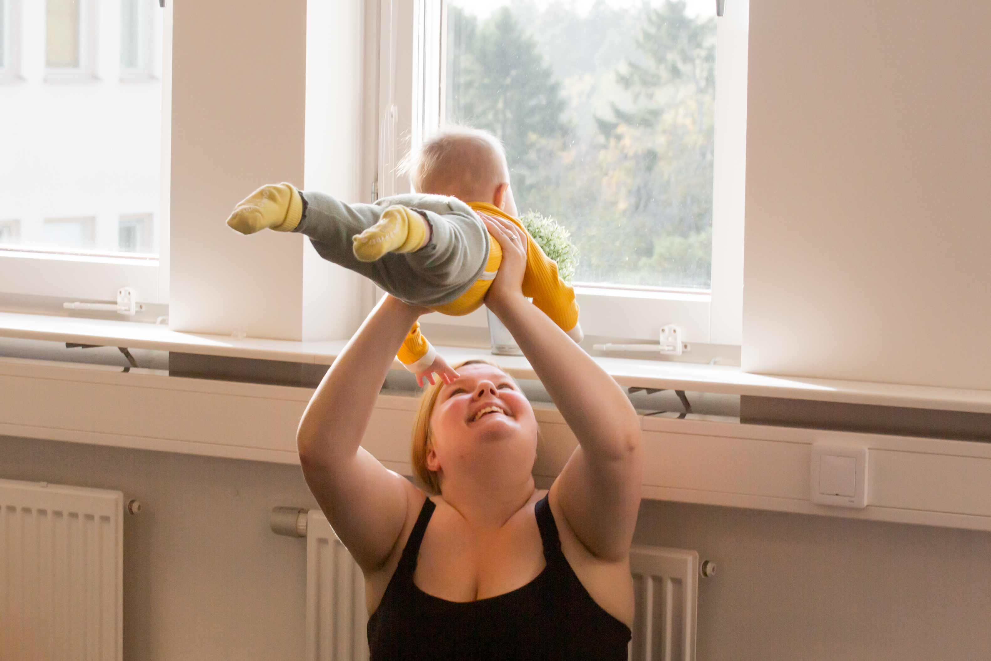 Mamma lyfter barn över huvudet och ler.