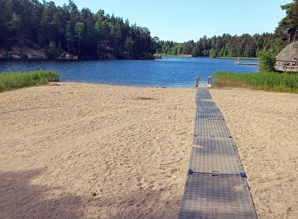 Badplats med sandstrand och en lång plastgång ner till vattnet.
