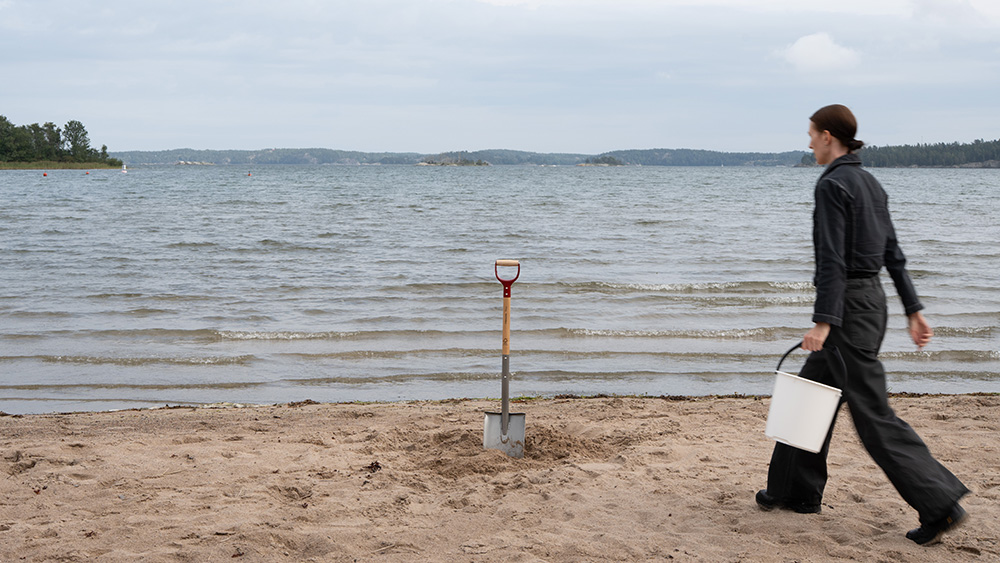 Kvinna med hink och spade på en strand.