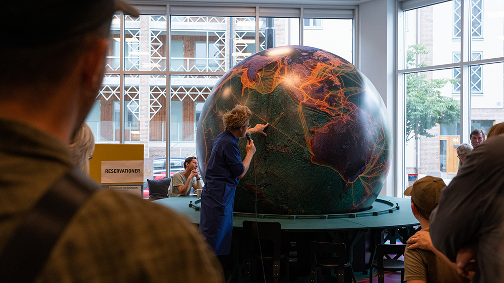 Stor jordglob i ett hörn av ett rum och en person som sträcker sig över jordgloben.